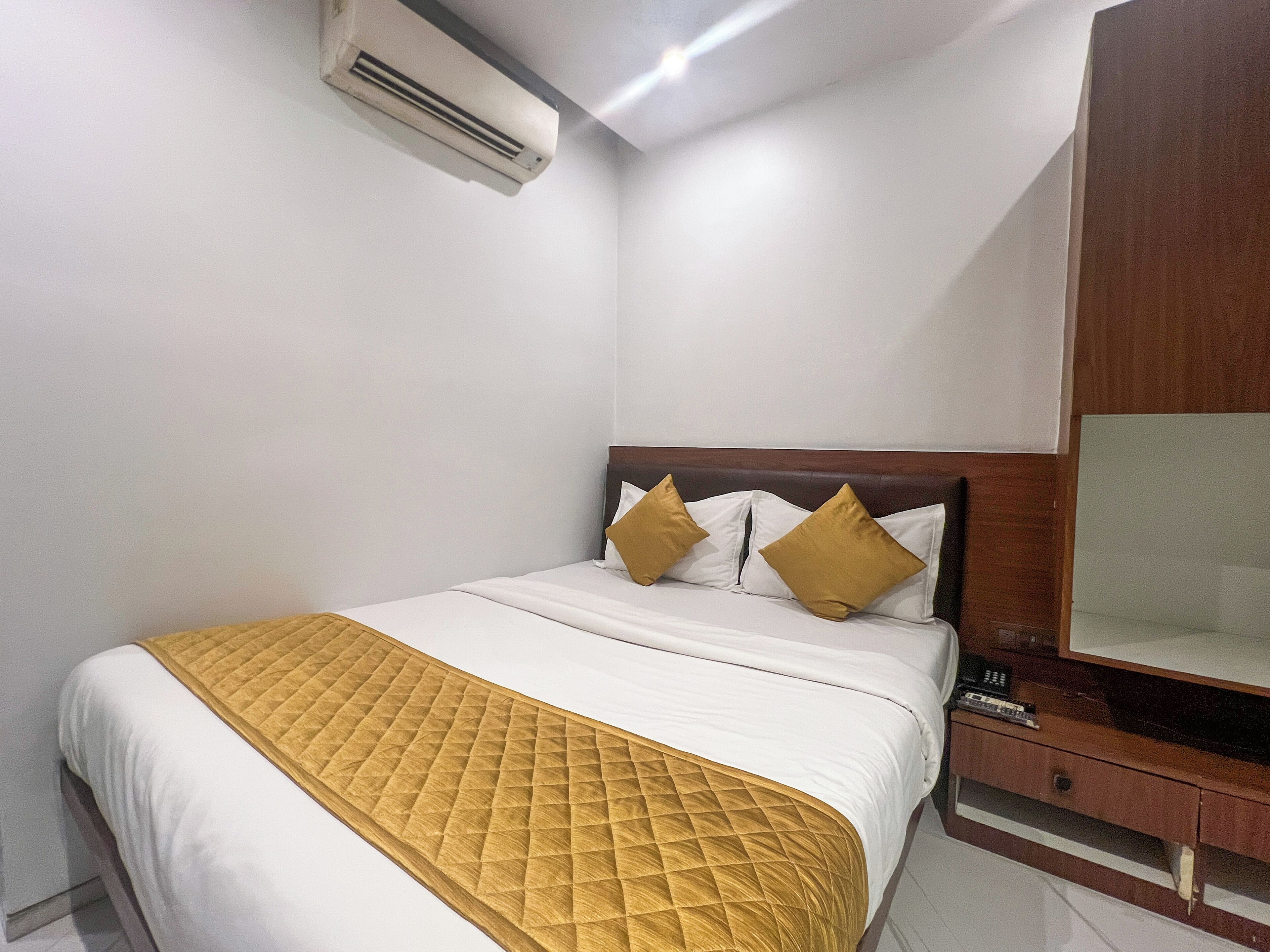 Habitación de hotel con una cama, una mesita de noche con teléfono y un aire acondicionado instalado en la pared.