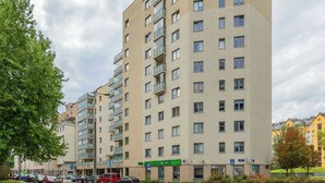 Un edificio residencial de varios pisos con balcones, un área de estacionamiento y un letrero verde que indica un establecimiento.
