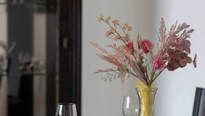 Una mesa de comedor dispuesta con platos, cubiertos y copas de vino, junto con un jarrón de flores.