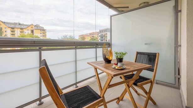 Un balcón con una mesa de madera y dos sillas, una maceta y un jarrón decorativo.