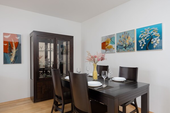A dining area with a dark wooden table, four chairs, a vase with flowers, and three paintings on the wall.