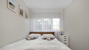 A bedroom with a bed, a nightstand, a lamp, and three framed pictures on the wall. - Intimate Apartment | Two Bedrooms, Work Desk (Wrocław)