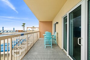 Een balkon met een zwembad, blauwe stoelen en uitzicht op het strand.