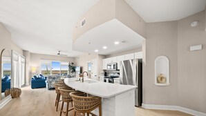 A modern kitchen with a large island, bar stools, and a view to the outside. - Sunrise Beach 501-Corner Views, FREE Beach Service, Heated Pool, FREE Perks! (Panama City Beach)