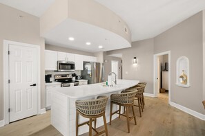 Una cocina moderna con armarios blancos, una isla central con taburetes altos y un techo curvo.