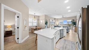 A modern kitchen with a central island, a dining area with a table and chairs, and a view of the outdoors. - Sunrise Beach 501-Corner Views, FREE Beach Service, Heated Pool, FREE Perks! (Panama City Beach)