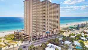 A high-rise hotel with multiple balconies, a beach view, and a parking area. - Sunrise Beach 501-Corner Views, FREE Beach Service, Heated Pool, FREE Perks! (Panama City Beach)