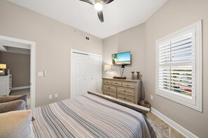 Un dormitorio con cama, cómoda, televisor y ventana con persianas.