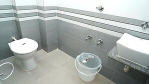 A small bathroom with a toilet, sink, and a bucket. - Hotel Nirali Rooms - Nexus Hospitality (Surat)