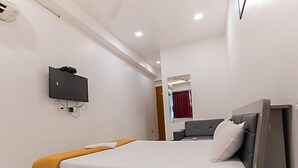 A hotel room with a bed, a bedside table, a telephone, and a television mounted on the wall. - Hotel Nirali Rooms - Nexus Hospitality (Surat)