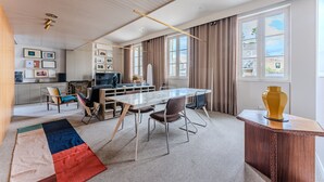 Uma sala de estar moderna com uma mesa grande, assentos confortáveis, uma televisão e vista para a cidade através de grandes janelas.