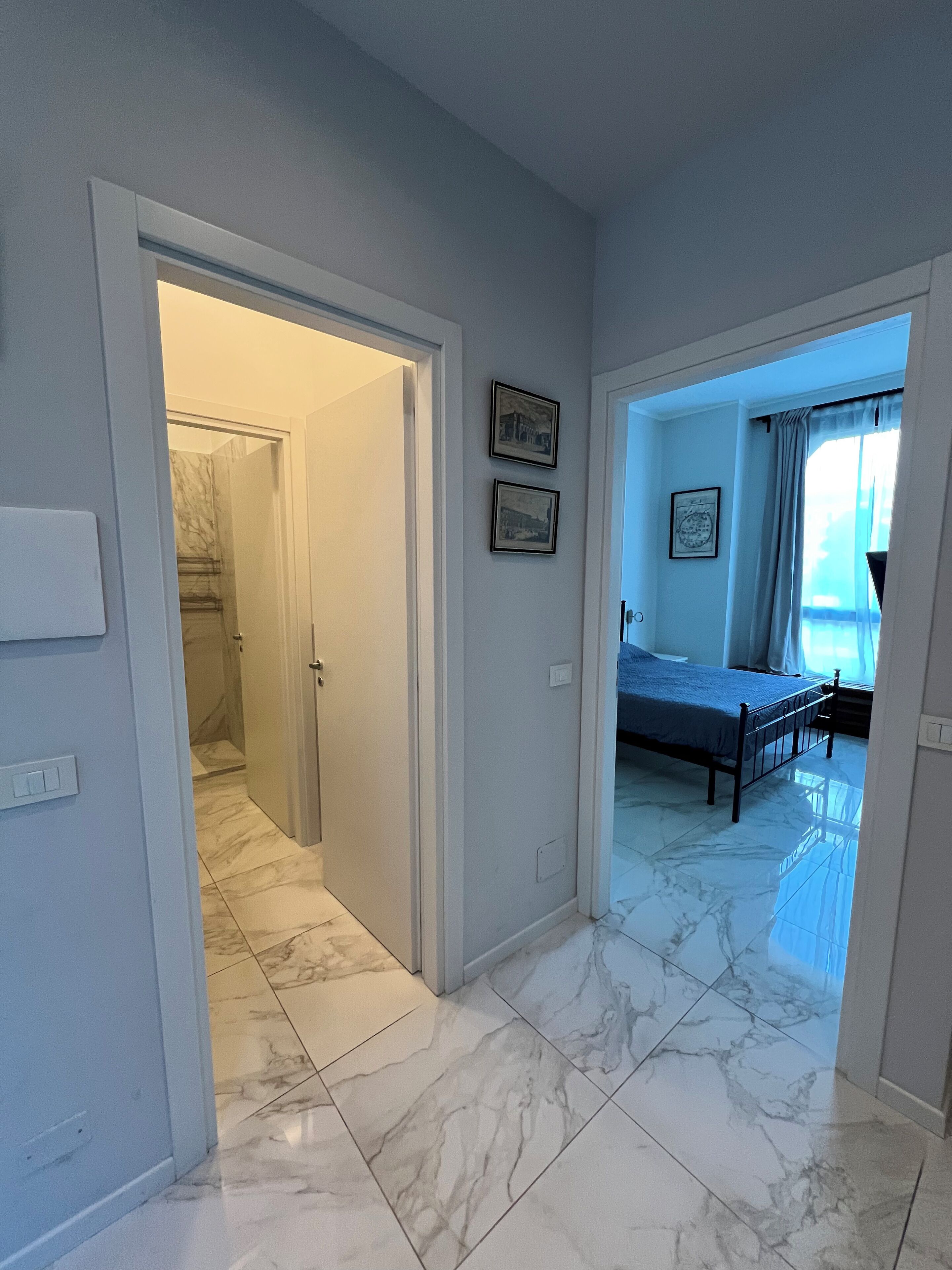 Una habitación de hotel con cama, baño con ducha y pasillo con puerta que da a otra habitación.