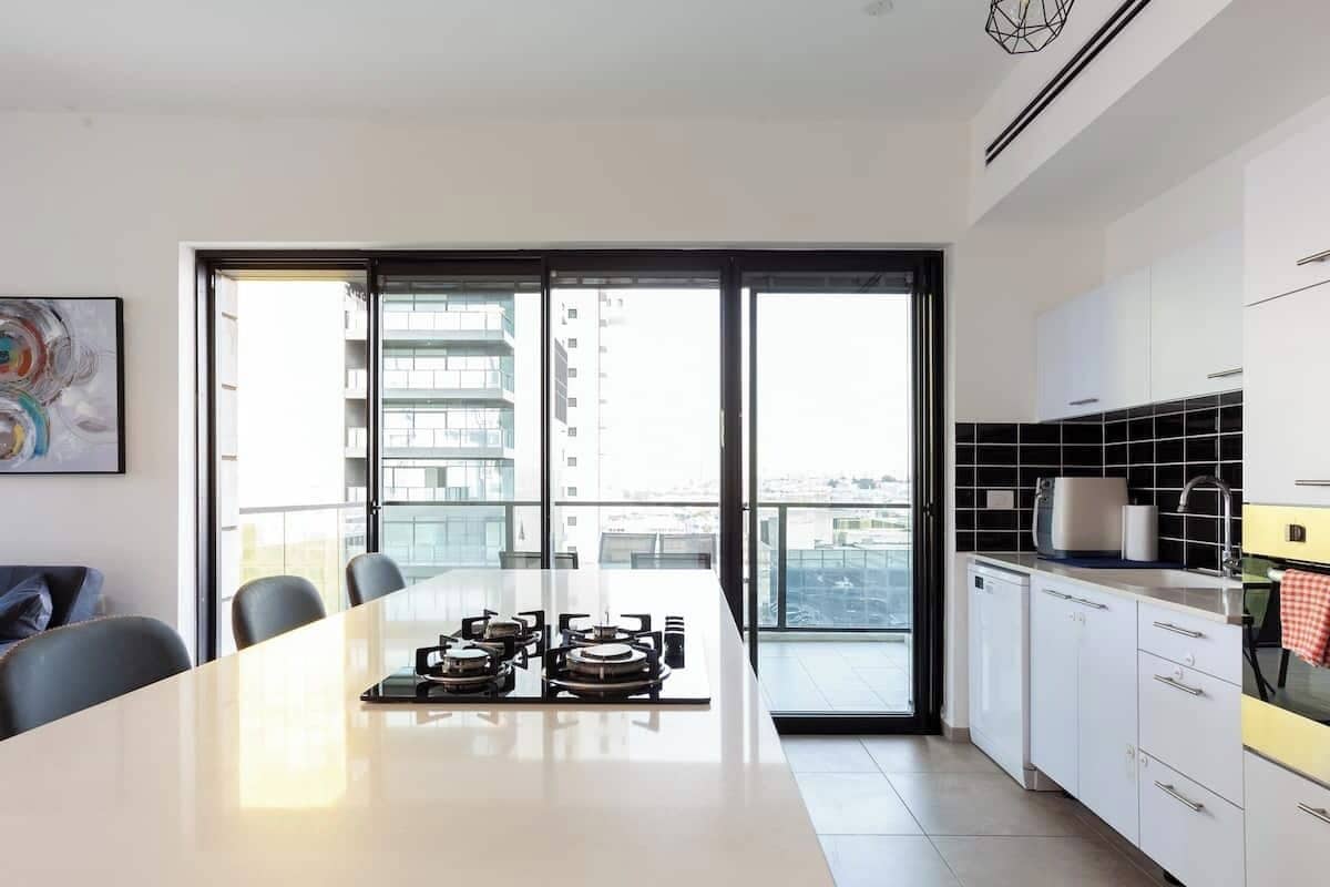 A modern kitchen with a large island, white cabinets, and a view of the city through large windows.