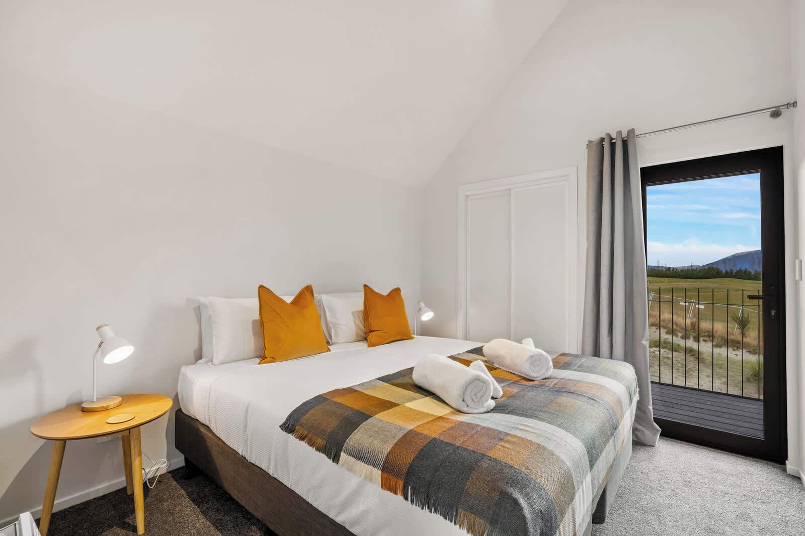 Un dormitorio con cama, mesita de noche, lámpara y vistas al exterior.