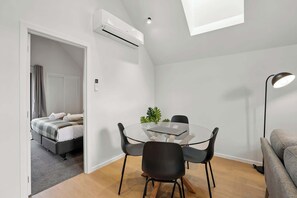 Una camera moderna e funzionale con un tavolo in vetro, sedie nere, un divano grigio, un condizionatore d'aria a soffitto e una piccola pianta sul tavolo.