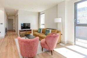 A modern living room with a sofa, two pink chairs, a TV, and a floor lamp. - The Stylish Nest in London (London)