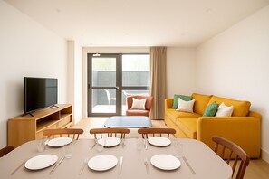 Een moderne woonkamer met een bank, televisie, eethoek en een schuifdeur naar een buitengebied.