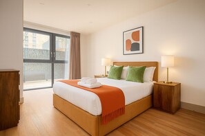 Een hotelkamer met een groot bed, twee nachtkastjes met lampen, een raam met gordijnen en een abstract kunstwerk in een lijst aan de muur.