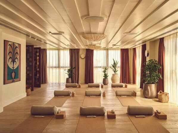 Een ruime kamer met houten vloeren, grote ramen voorzien van gordijnen, en meerdere massagebedden klaar voor gasten.