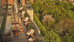 Eine Dachterrasse mit Sitzgelegenheiten im Freien, Topfpflanzen und Blick auf eine Wohngegend.