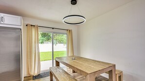 Een moderne keuken met een houten tafel en bank, een koelkast, en een schuifdeur naar een groen buitenverblijf.