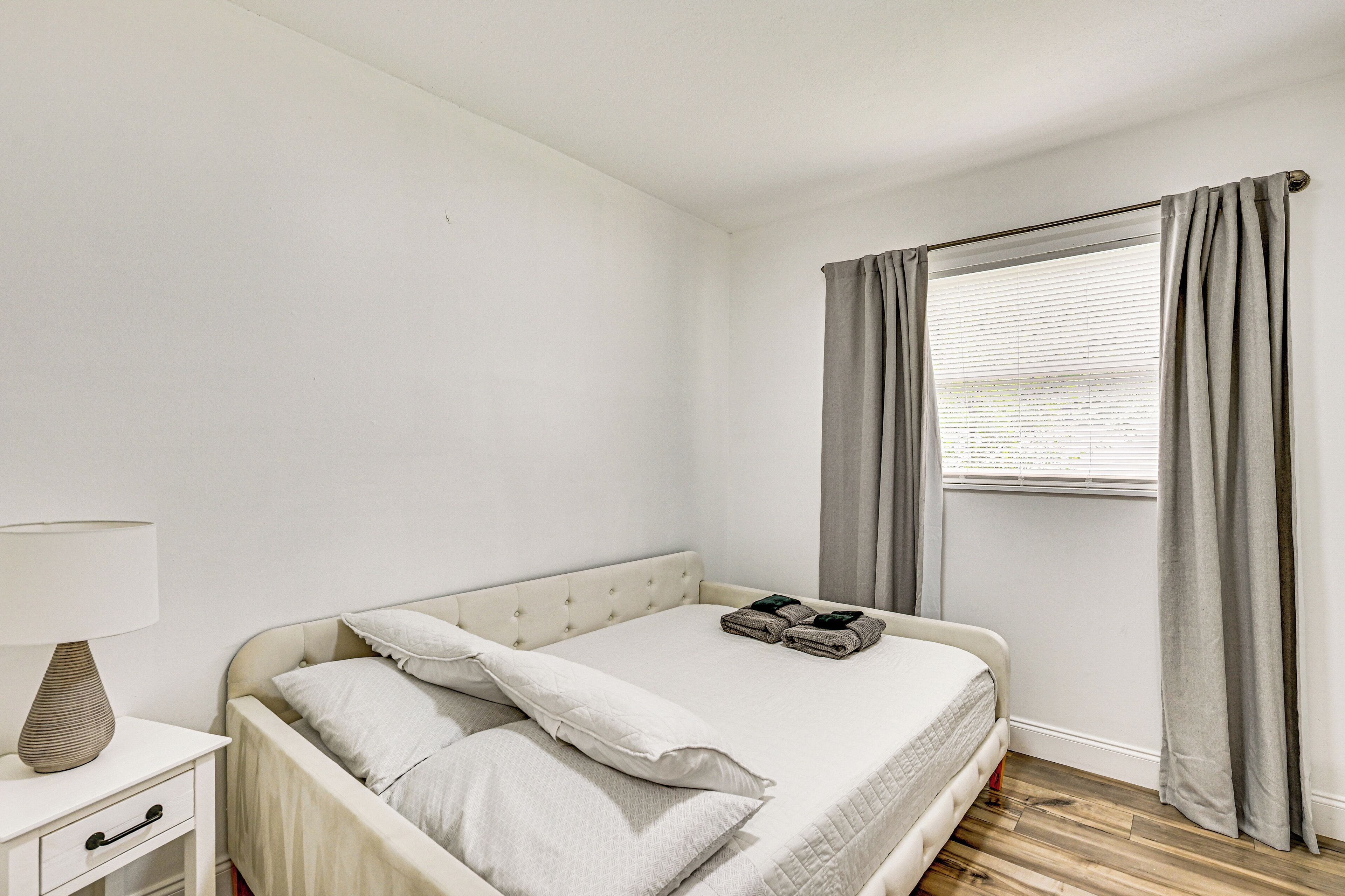 Un dormitorio con cama, mesita de noche, lámpara y ventana con cortinas.