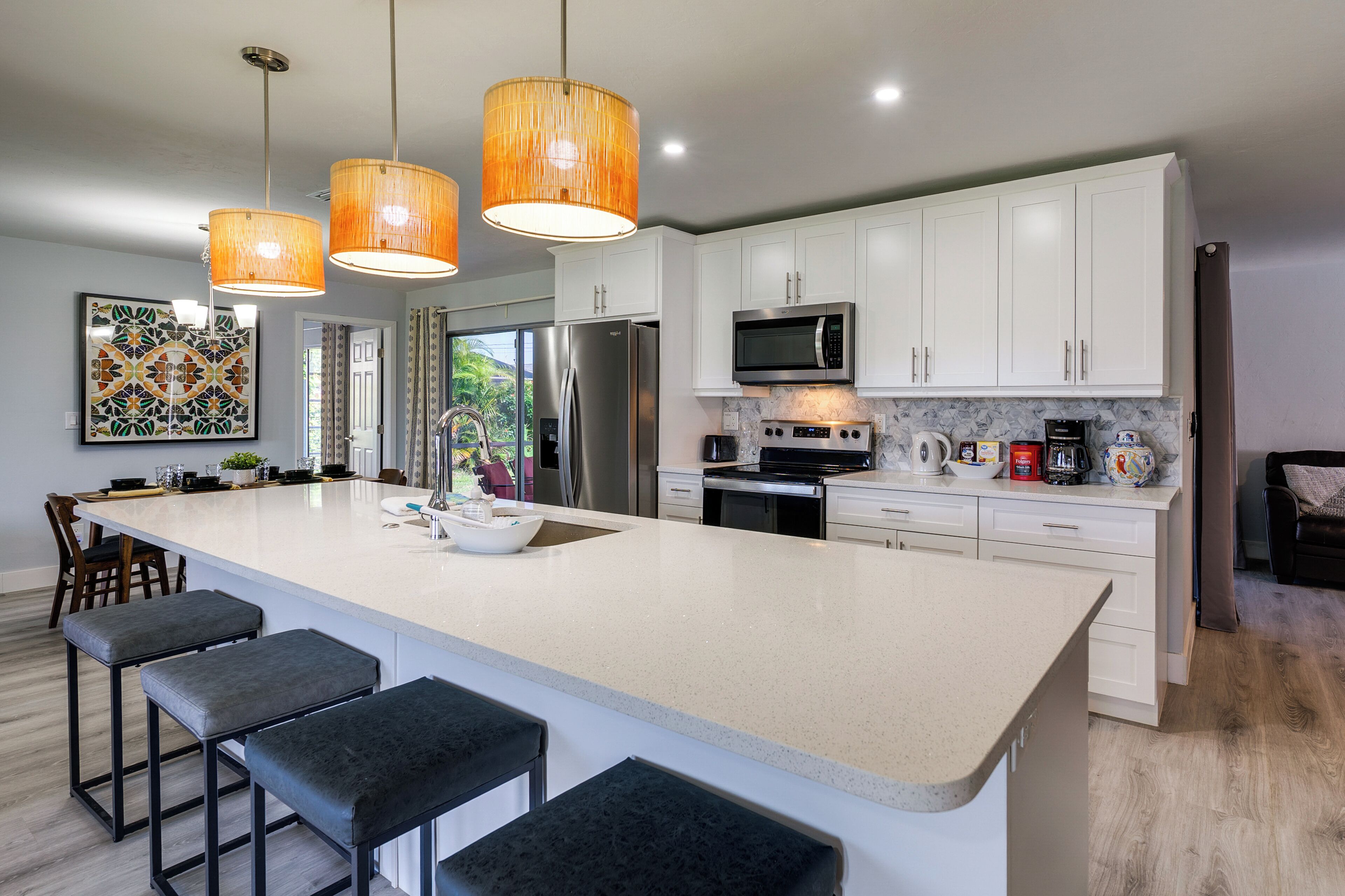 A modern kitchen with a large island, white cabinets, stainless steel appliances, and pendant lighting.