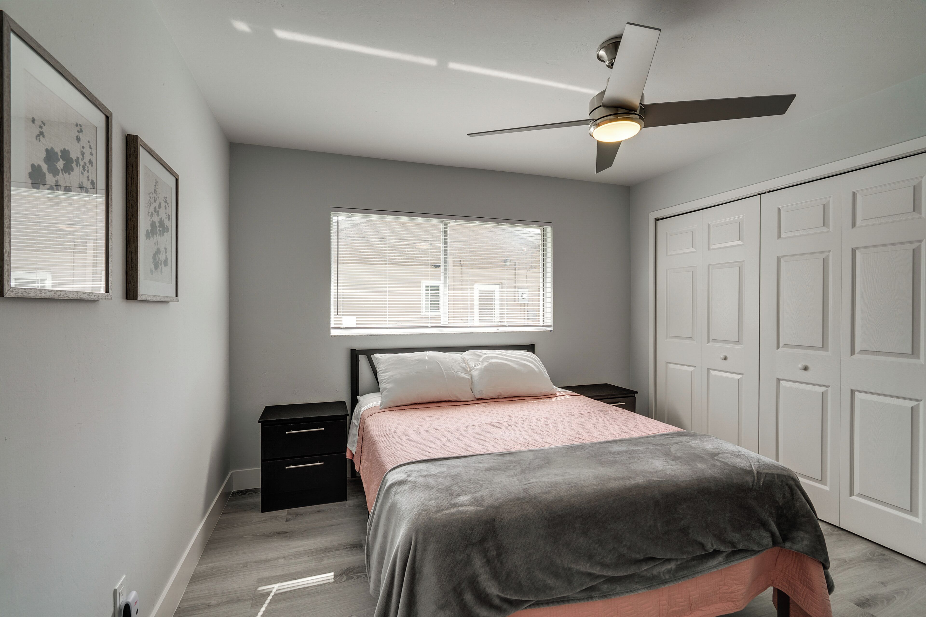 A bedroom with a bed, a nightstand, a ceiling fan, a window with blinds, and a wardrobe.
