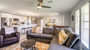 A modern living room with a sofa, armchair, and coffee table, a kitchen in the background, and a ceiling fan. - Game, Shop & Beach-hop: Family Home in Cape Coral (Cape Coral)