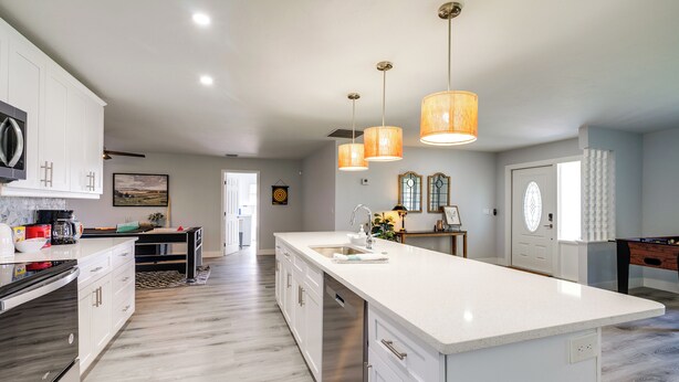 A modern kitchen with white cabinetry, a large island with a sink, and pendant lighting. - Game, Shop & Beach-hop: Family Home in Cape Coral (Cape Coral)