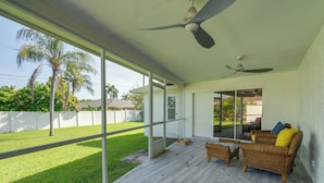 A covered patio with wicker furniture, a ceiling fan, and a view of a green lawn and palm trees. - Game, Shop & Beach-hop: Family Home in Cape Coral (Cape Coral)