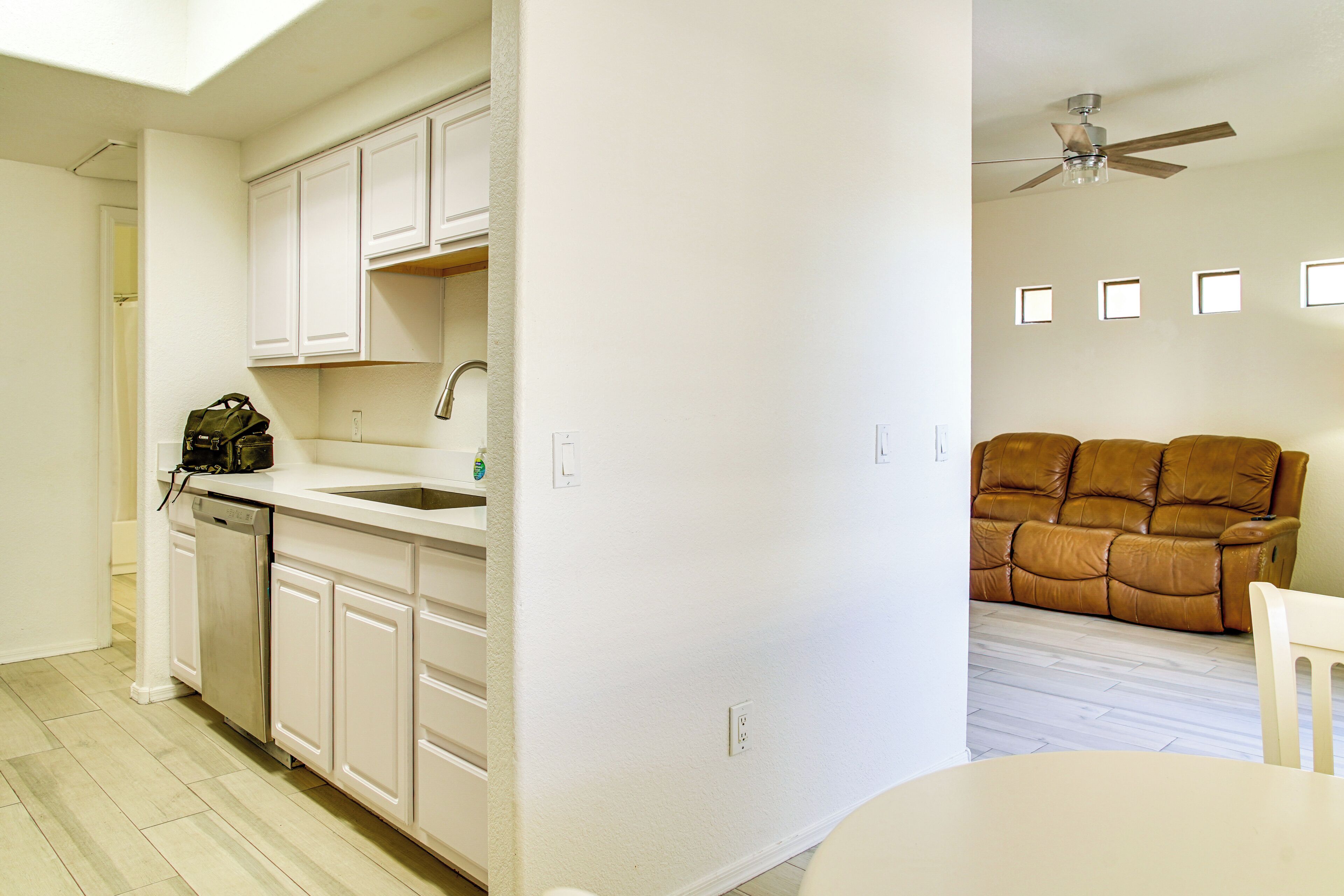 A modern kitchen with white cabinetry, a dishwasher, and a brown leather sofa in the adjacent living area.