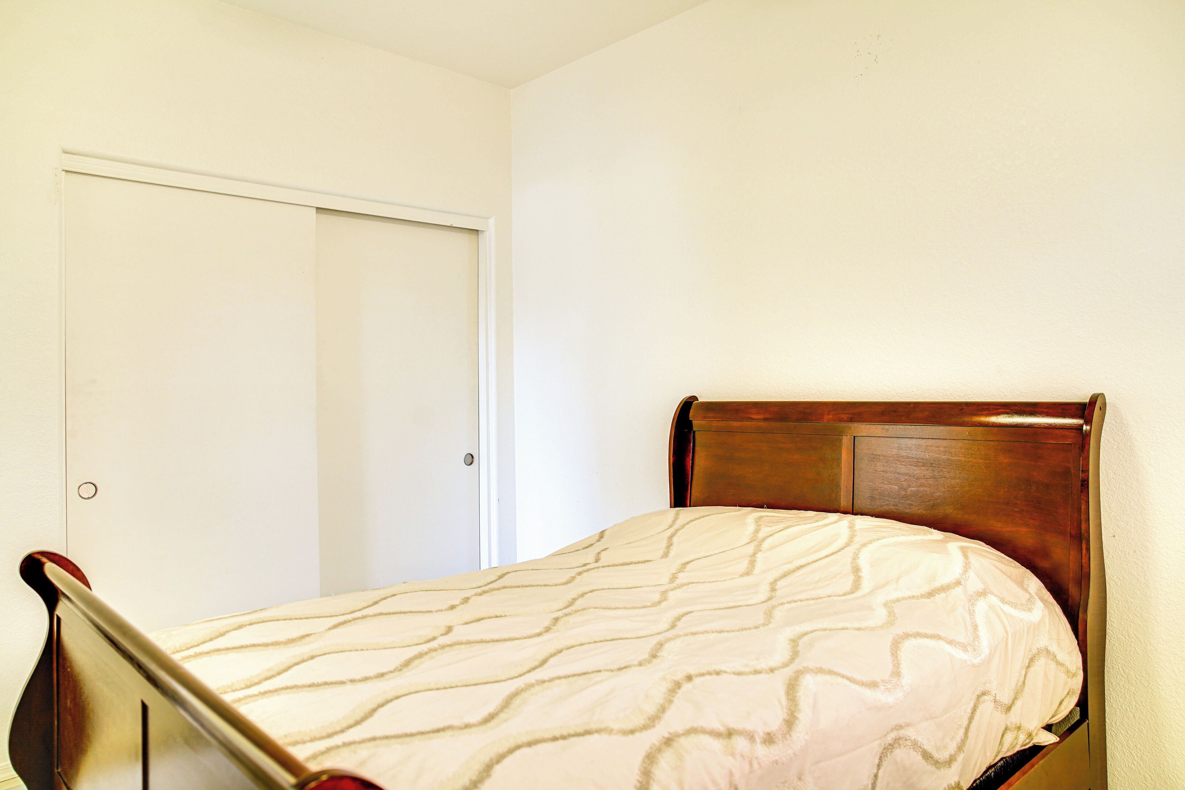 Una cama individual con cabecera de madera en una habitación con paredes blancas y una puerta cerrada.