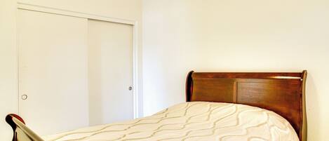 Una cama individual con cabecera de madera en una habitación con paredes blancas y una puerta cerrada.