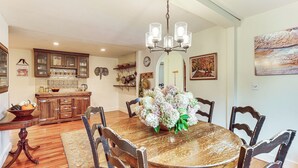 Un coin repas avec une table en bois, des chaises, un lustre et un vase de fleurs.