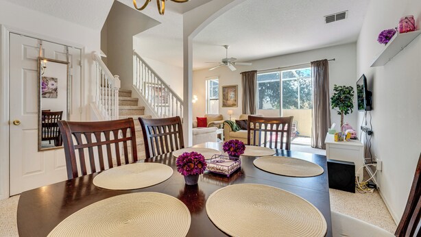 A dining area with a dark wooden table, woven placemats, and two potted plants with purple flowers. - 10 Mi to Disney World: Townhome w/ Community Pool! (Kissimmee)