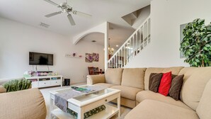 A living room with a beige sofa, a coffee table, a TV, and a staircase leading to another level. - 10 Mi to Disney World: Townhome w/ Community Pool! (Kissimmee)