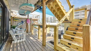 Eine Holzterrasse mit einem weißen Sofa, einem kleinen Tisch, einer Treppe und Blick auf die Stadt.