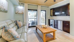 Ein Wohnzimmer mit einer Couch, einem Holztisch und einer Küchenzeile mit dunklen Schränken und einem Einbauofen.