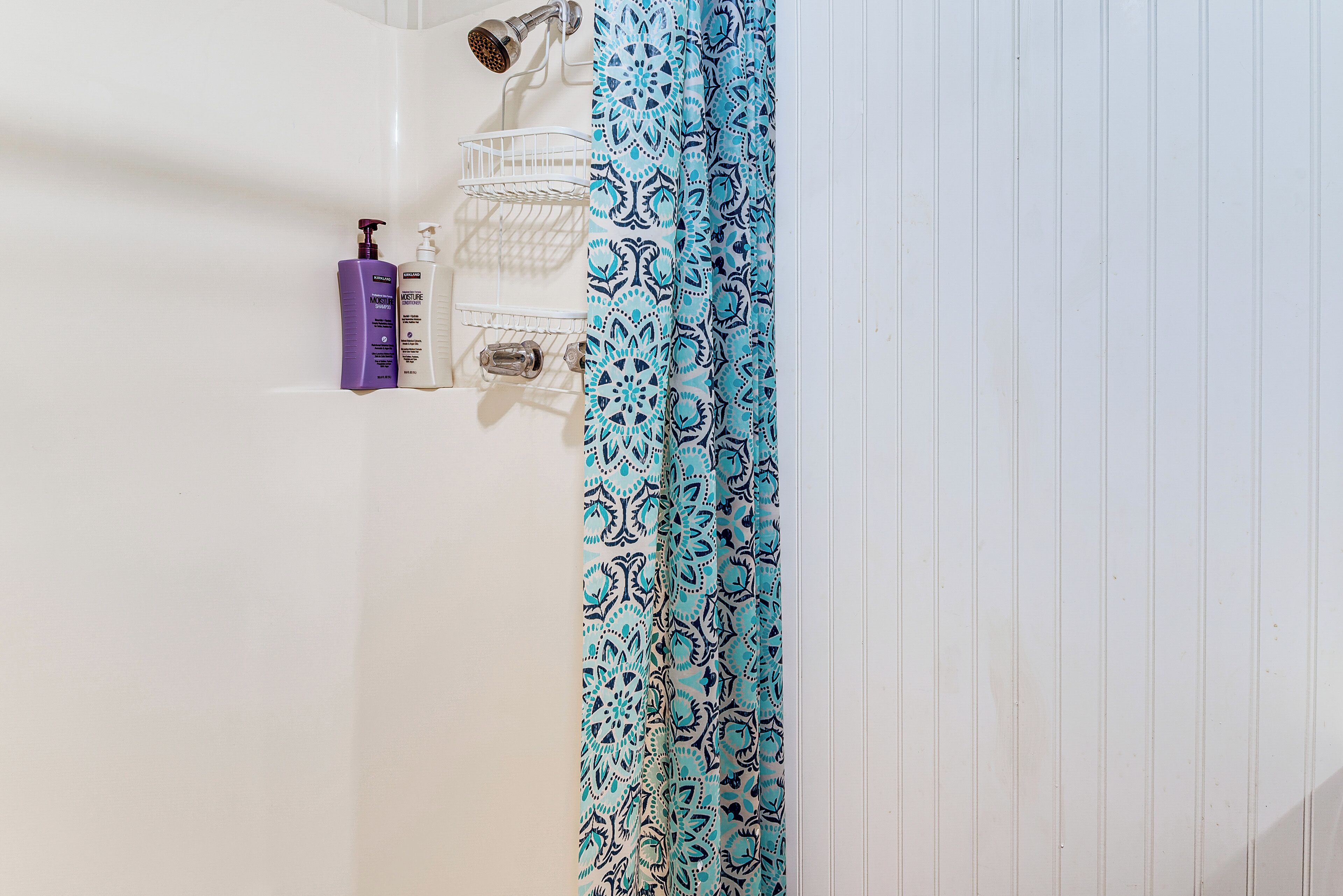 Une salle de bain avec un mur blanc, un rideau de douche bleu à motifs et deux bouteilles de shampoing posées sur une étagère.