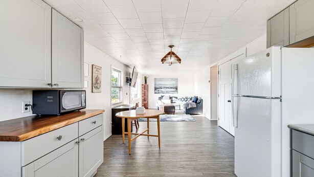 Ett kök med vita skåp, en bänkskiva i trä, en mikrovågsugn, ett matbord och ett kylskåp.