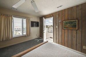 Una camera da letto con un letto, una finestra con tende, una porta che dà sull'esterno, una ventola a soffitto e un quadro appeso al muro.