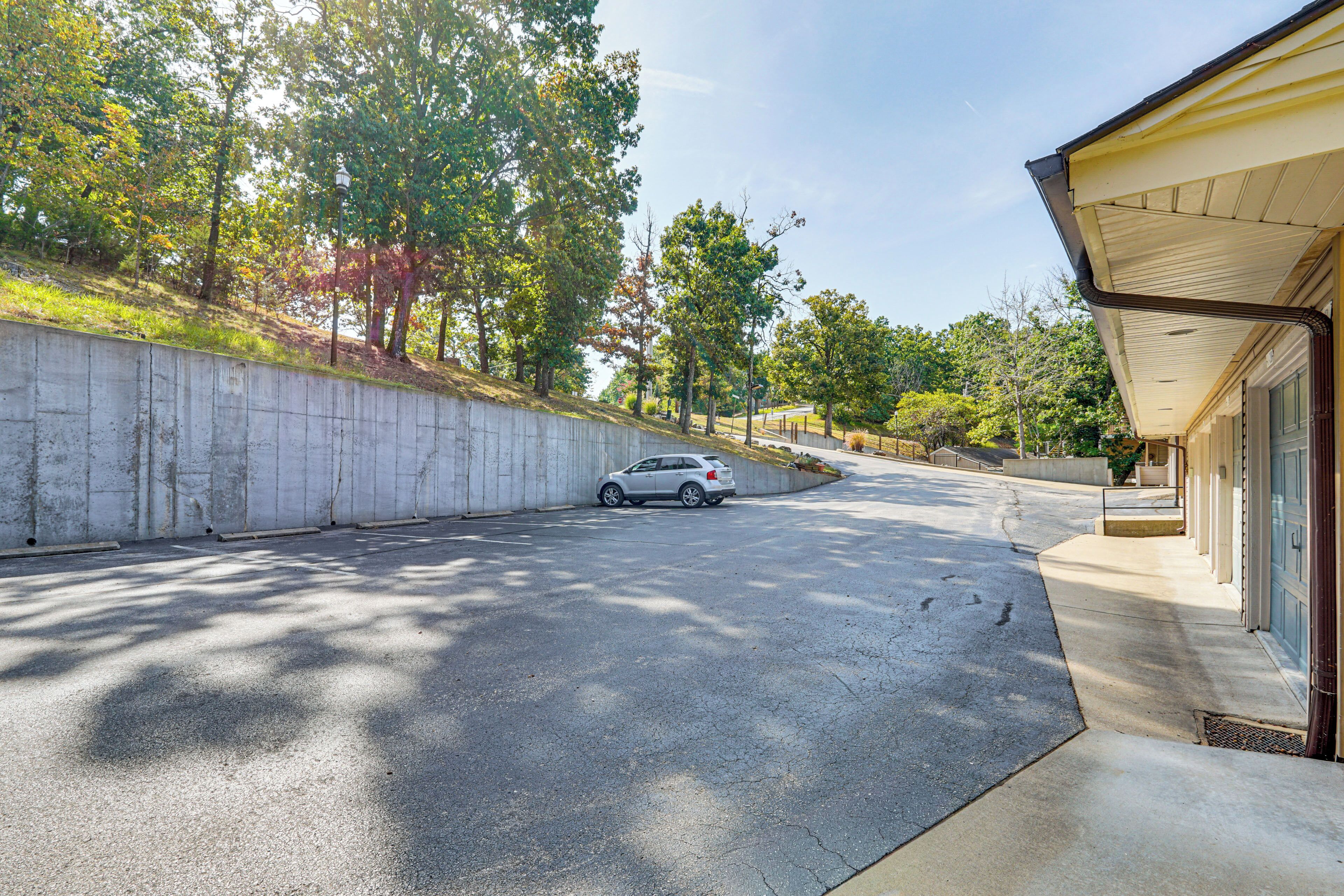 A residential driveway with a parked car, a concrete retaining wall, and a house with a garage.