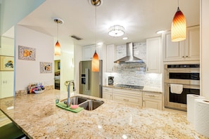 Eine moderne Küche mit Granit Arbeitsplatten, Edelstahlgeräten, Pendelleuchten und einer Rückwand mit Mosaikfliesenmuster.