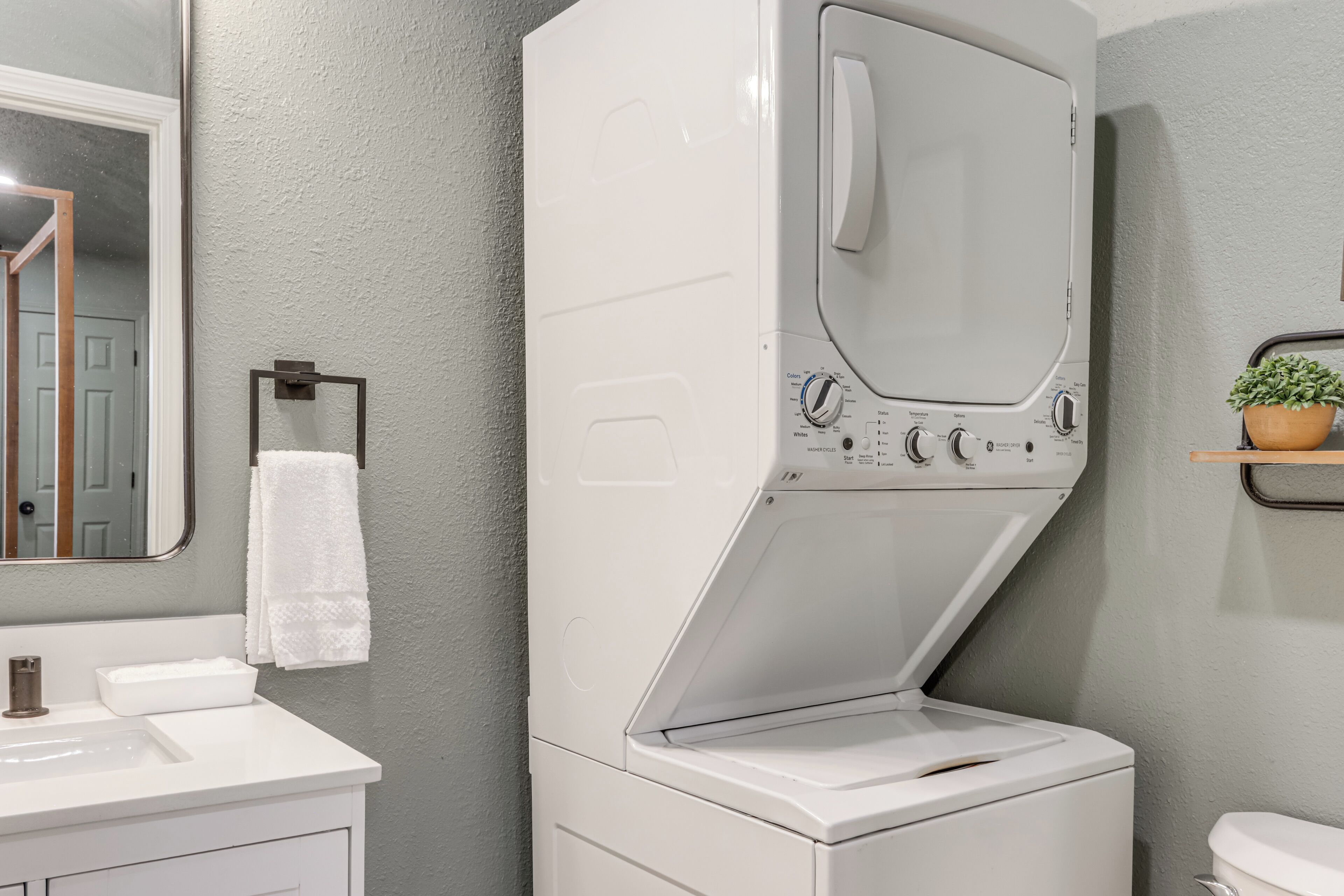 A compact, modern bathroom with a built-in washer and dryer, a white sink, and a mirror.
