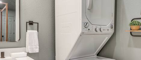 A compact, modern bathroom with a built-in washer and dryer, a white sink, and a mirror.