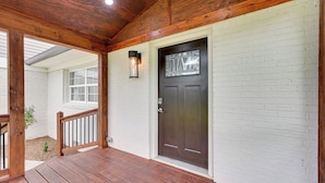 A wooden porch with a dark brown door and white brick walls.
