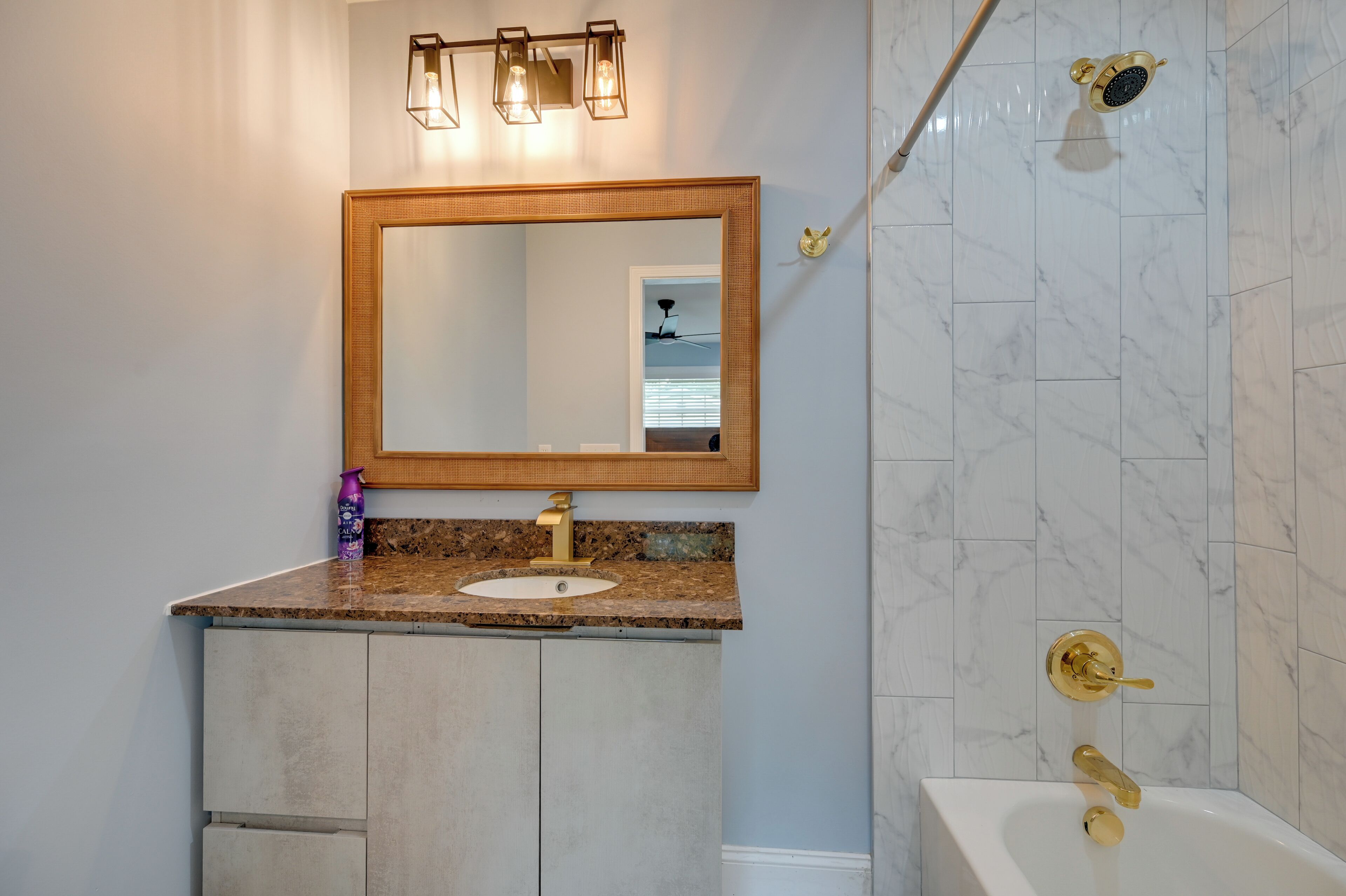 A bathroom with a marble-tiled shower, a sink with a gold faucet, and a mirror with a wooden frame.