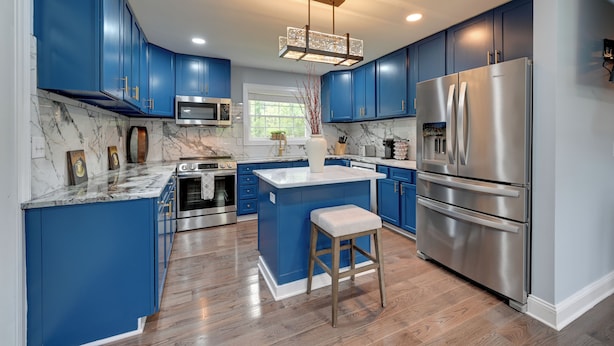 A modern kitchen with blue cabinets, a stainless steel refrigerator, and a marble countertop.