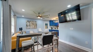 A modern kitchen with a flat-screen TV, a ceiling fan, and a dining area with a table and chairs.